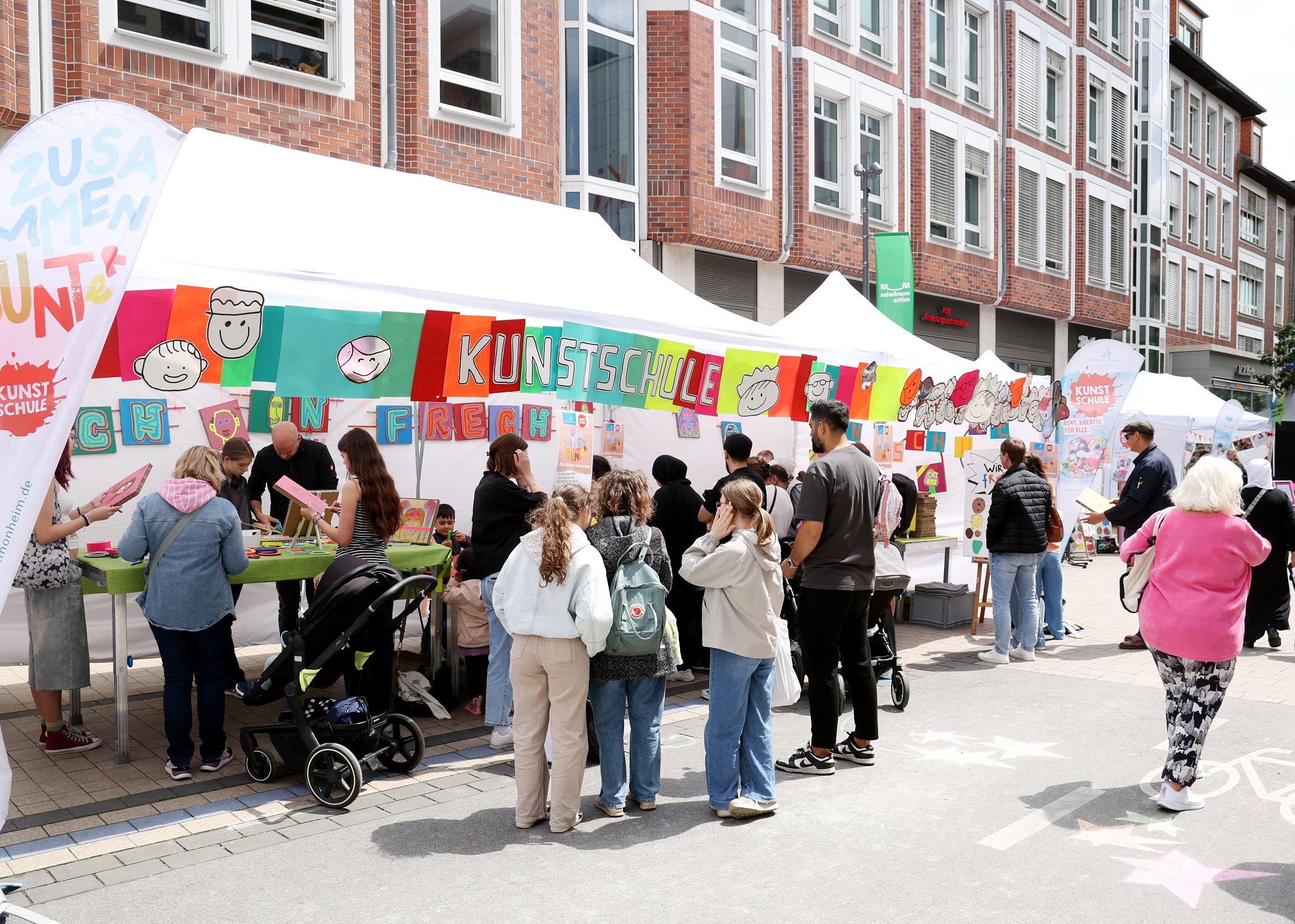 Blick auf den bunten Stand der Kunstschule. Unter den Pavillons und davor sind viele Menschen.